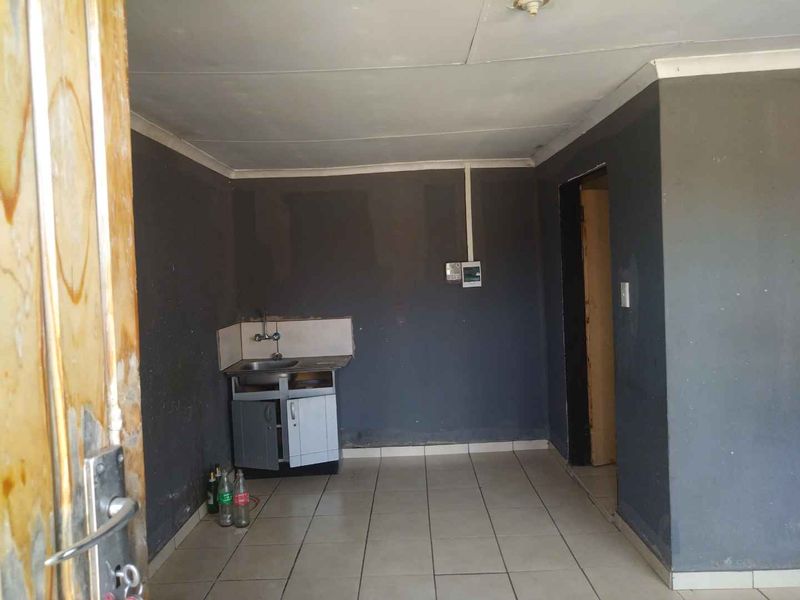 A small, basic kitchen area featuring tiled flooring, a single sink unit with base cabinetry, and dark painted walls requiring maintenance.