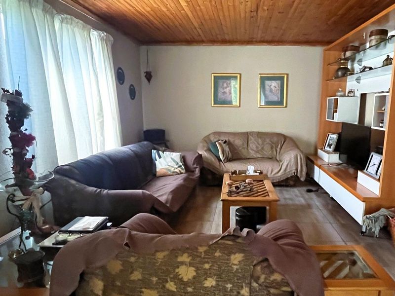 A living room featuring a timber-clad ceiling, tiled flooring, and a large built-in shelving unit.