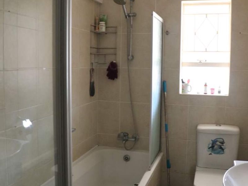 A functional bathroom featuring a combined bathtub and shower, tiled walls and flooring, and a standard toilet.