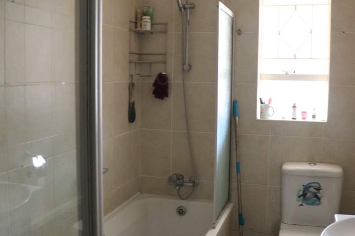 A functional bathroom featuring a combined bathtub and shower, tiled walls and flooring, and a standard toilet.
