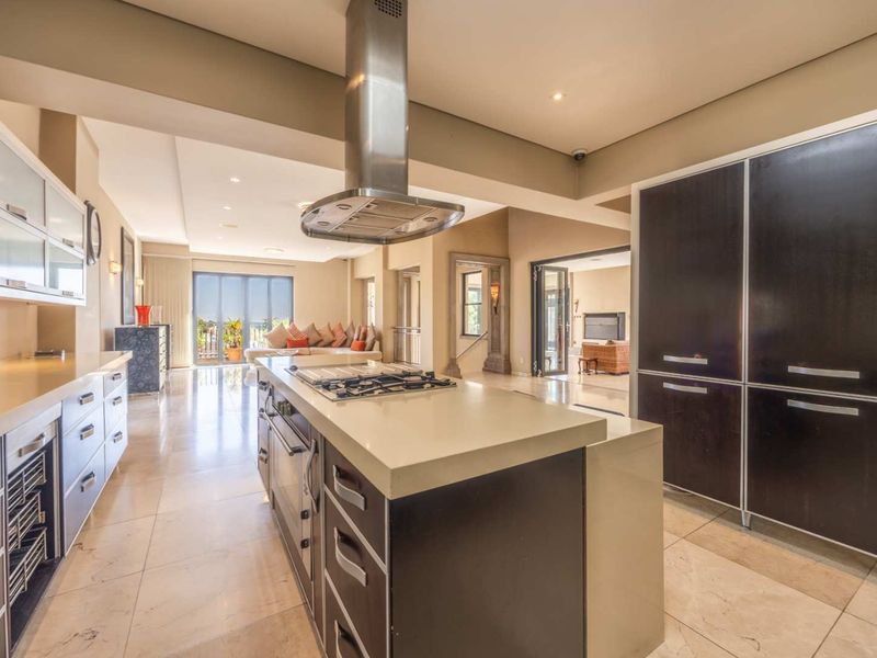 Spacious open-plan kitchen featuring a central island with gas cooktop, stainless steel extractor, stone countertops, and sleek built-in cabinetry, flowing into the living area.