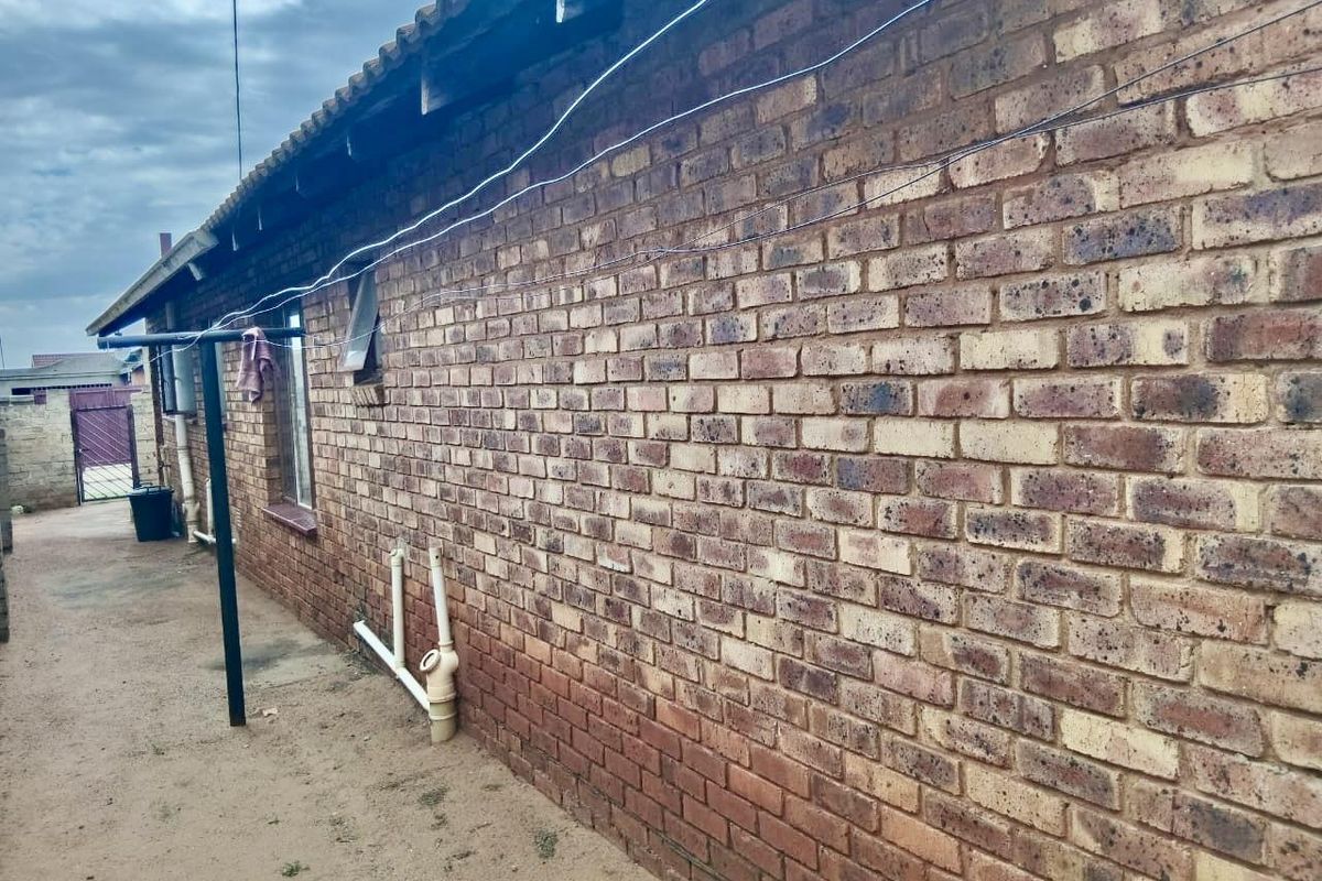 Exterior view of the rear brick facade showing exposed plumbing, overhead wiring, and weathered roof fascia.