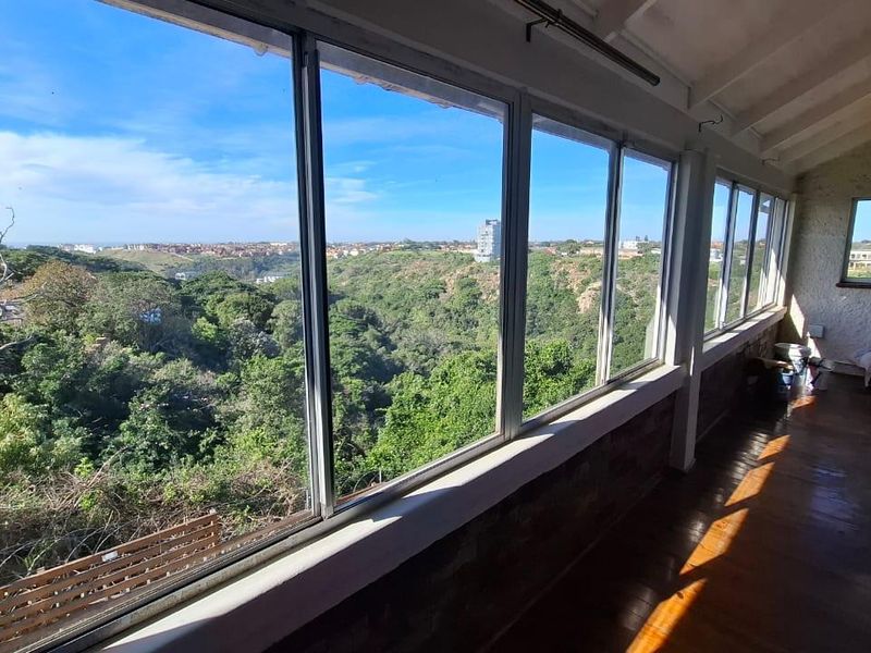Enclosed balcony featuring expansive windows with scenic valley views, timber flooring, and exposed beam ceilings, offering a bright and versatile space.