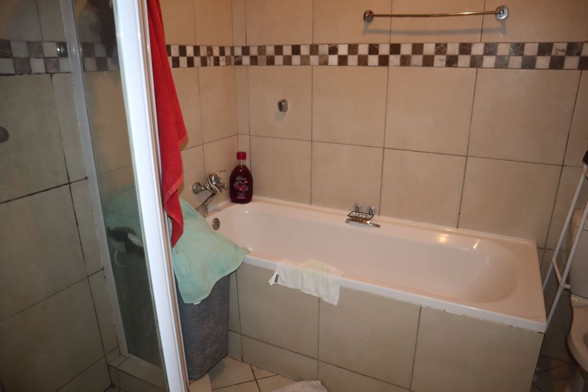 A functional bathroom featuring a built-in bathtub, a separate shower enclosure, and neutral ceramic wall tiling with a decorative border.