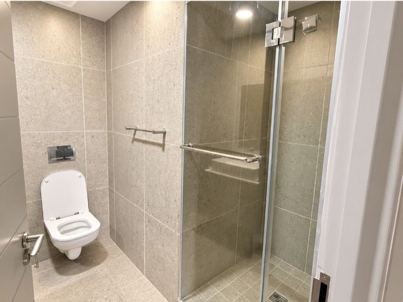 Modern bathroom featuring a wall-mounted toilet, a glass-enclosed shower, and neutral floor-to-ceiling tiling with recessed lighting.
