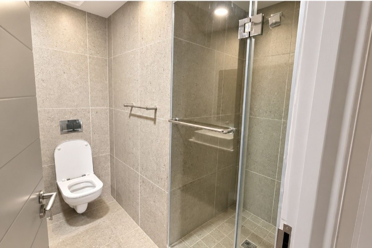 Modern bathroom featuring a wall-mounted toilet, a glass-enclosed shower, and neutral floor-to-ceiling tiling with recessed lighting.