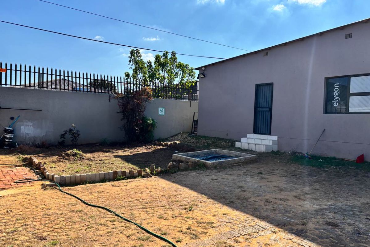 Rear exterior view of the property featuring a paved area, a small raised garden bed, and a perimeter wall with security spikes.