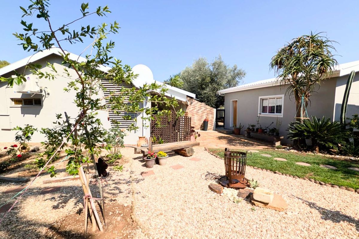 A well-maintained rear garden area featuring gravel landscaping, established trees, and access to the main dwelling and secondary structure.