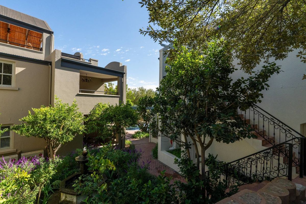 A view of the apartment complex exterior featuring landscaped gardens, paved walkways, and external staircases with decorative wrought iron railings.