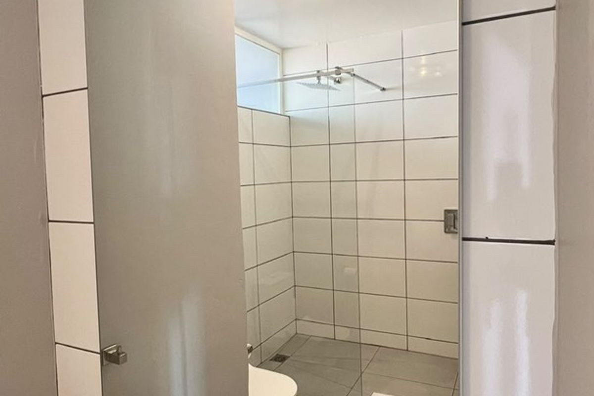 Modern bathroom featuring a wall-mounted basin with chrome tap, large mirror, and a walk-in shower with glass screen and white tiled walls.