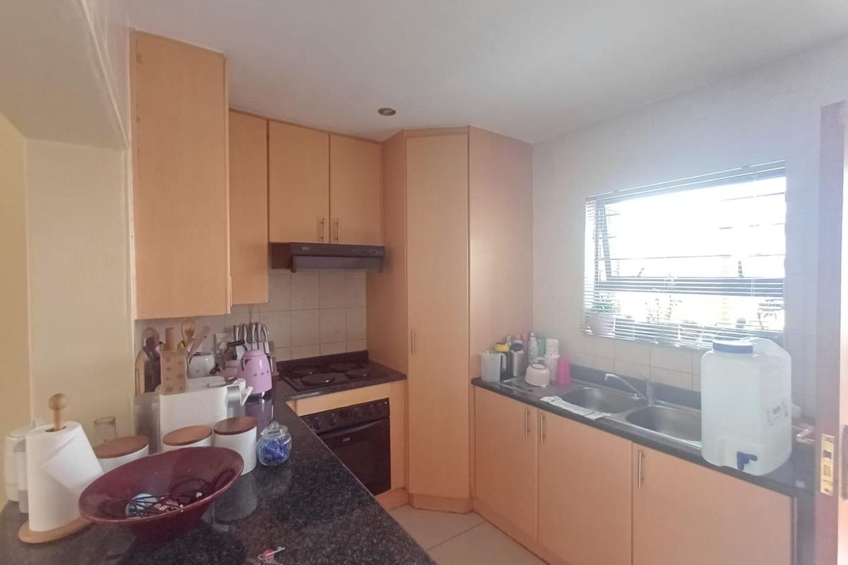 A functional kitchen featuring light wood cabinetry, granite countertops, a built-in oven, electric hob, and a double basin sink with a tiled backsplash.