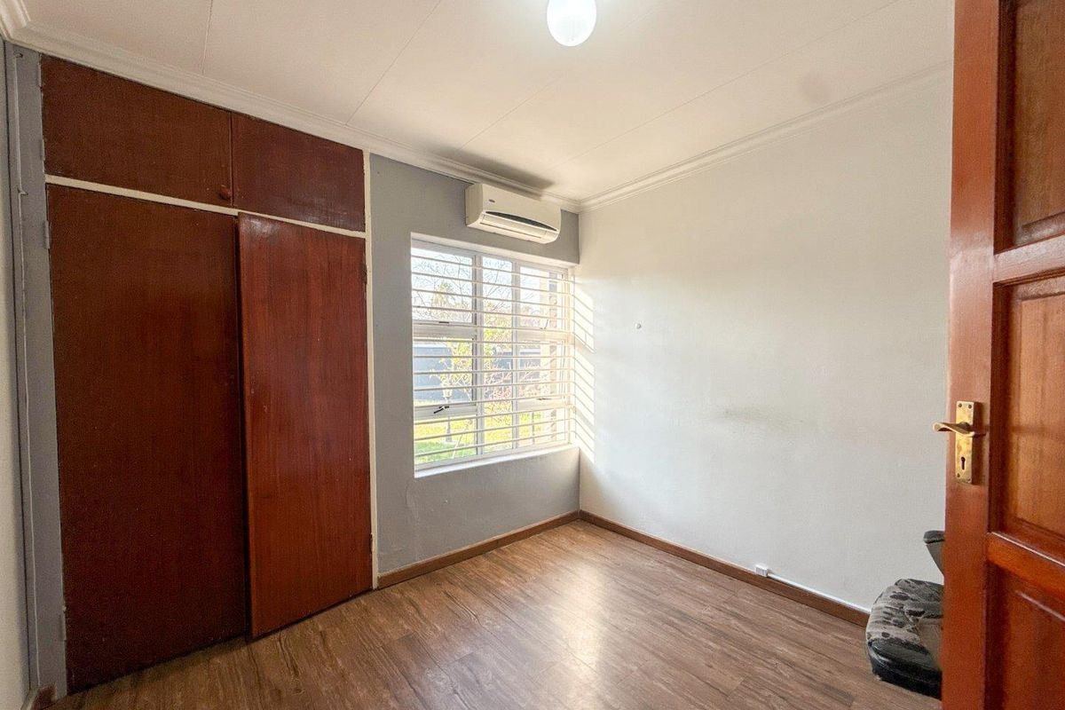 A functional bedroom featuring laminate flooring, built-in wooden cupboards, and a wall-mounted air conditioning unit, offering a clean and versatile space.