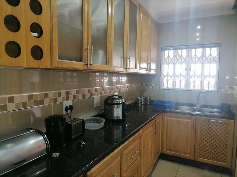 A functional kitchen featuring wooden cabinetry, granite countertops, a double basin sink, and a tiled backsplash with a window security gate.
