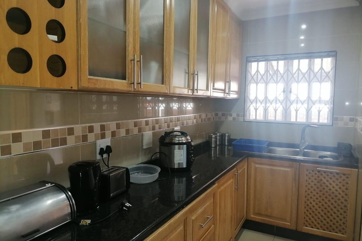 A functional kitchen featuring wooden cabinetry, granite countertops, a double basin sink, and a tiled backsplash with a window security gate.