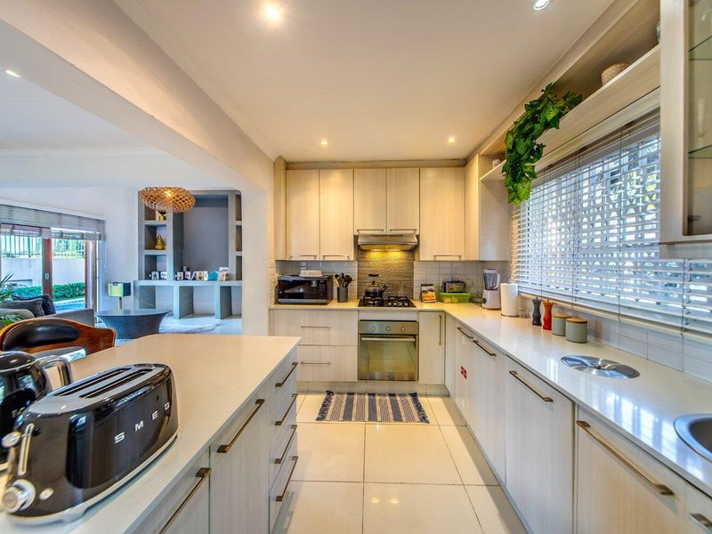 Modern kitchen featuring light wood cabinetry, stone countertops, integrated gas hob, built-in oven, and recessed lighting, seamlessly flowing into the adjacent living area.