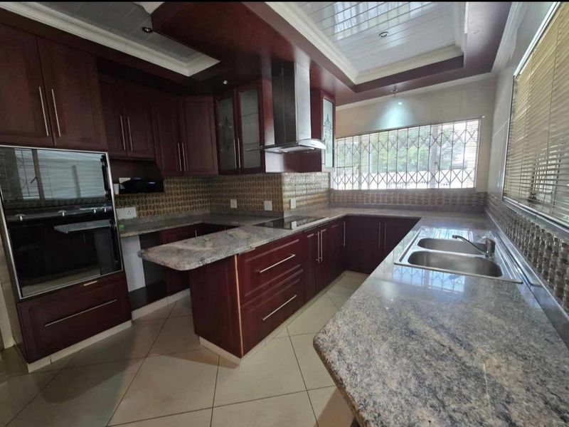 A spacious kitchen featuring dark wood cabinetry, granite countertops, a built-in oven, extractor fan, and a double sink with tiled flooring.