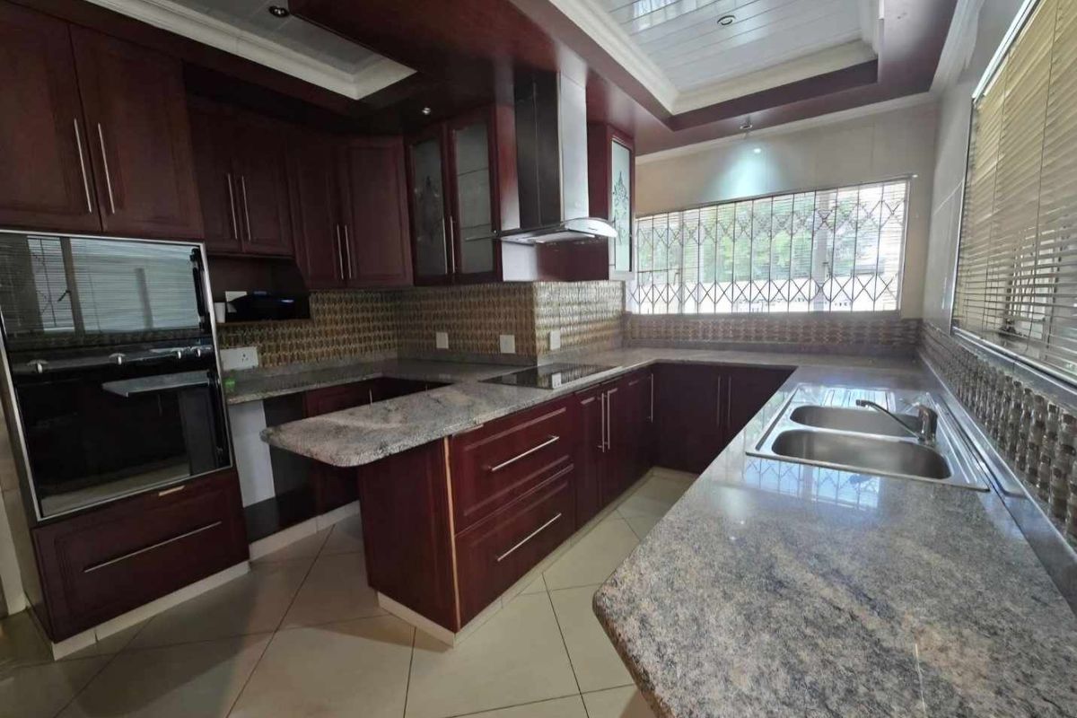 A spacious kitchen featuring dark wood cabinetry, granite countertops, a built-in oven, extractor fan, and a double sink with tiled flooring.