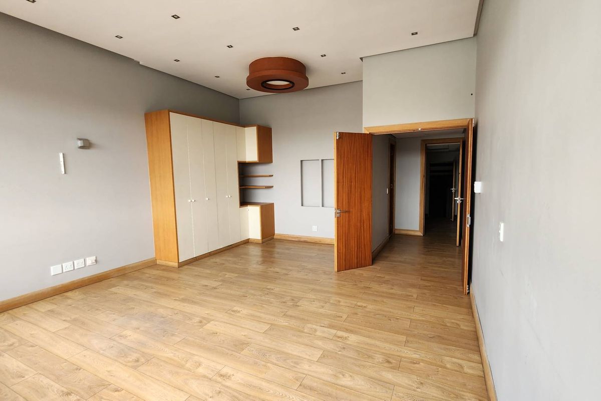 Spacious bedroom featuring light laminate flooring, neutral grey walls, and a large built-in wardrobe with integrated shelving.