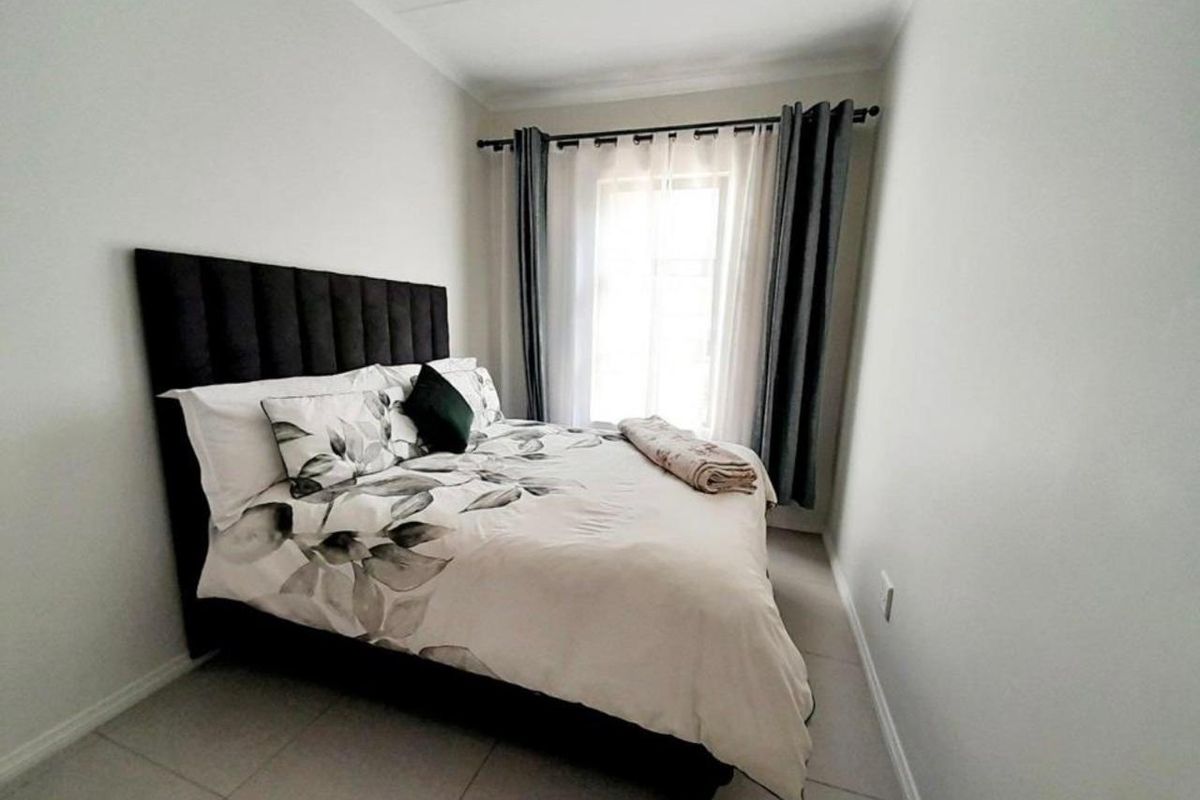 A well-lit bedroom featuring neutral floor tiles, clean wall finishes, and a window with curtain rod installation.