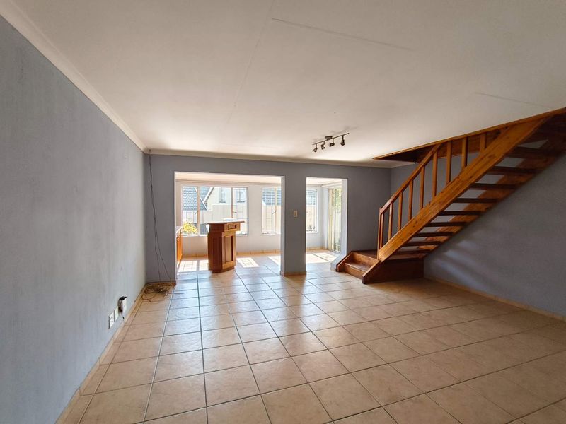 Spacious open-plan living area featuring tiled flooring, a wooden staircase, and a built-in bar counter, offering a versatile layout for modern living.