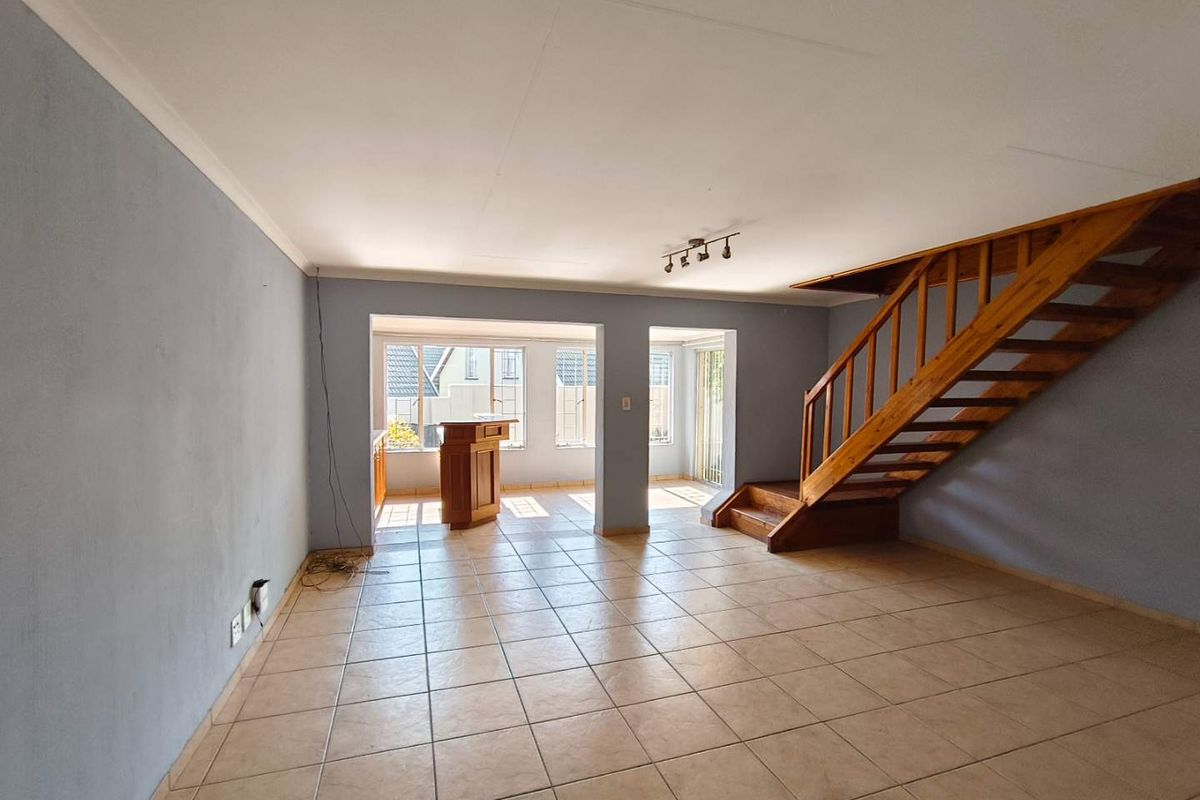 Spacious open-plan living area featuring tiled flooring, a wooden staircase, and a built-in bar counter, offering a versatile layout for modern living.
