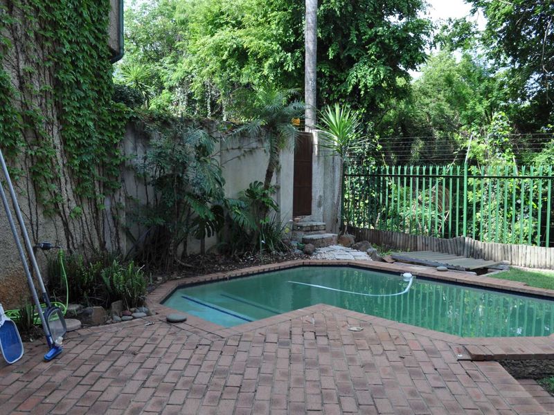 Private outdoor pool area featuring brick paving, perimeter wall with electric fencing, and established garden surroundings.