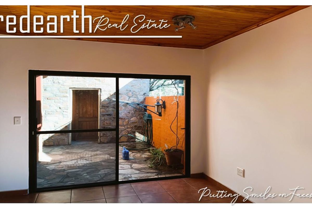 An empty living room featuring a timber ceiling, tiled floors, and a large sliding glass door providing access to an outdoor patio area.