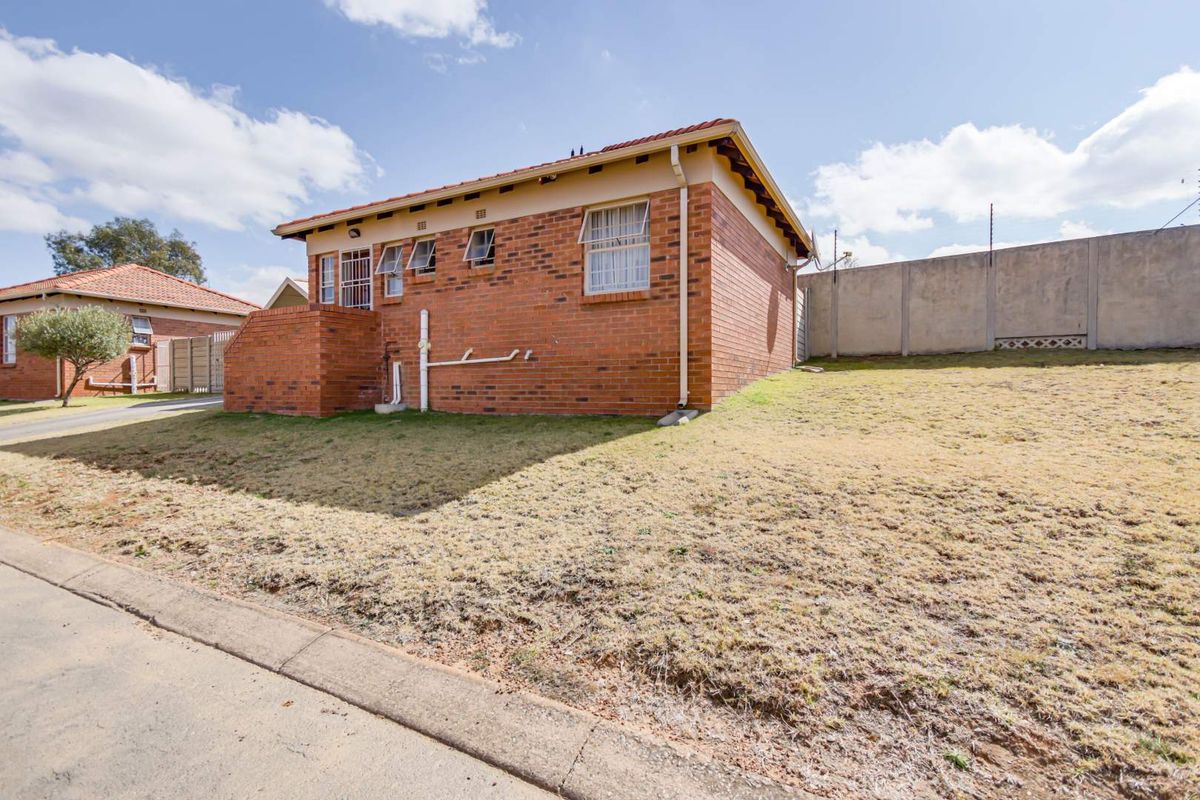 Side view of a face-brick residential house featuring tiled roofing, security window bars, and a perimeter concrete boundary wall.