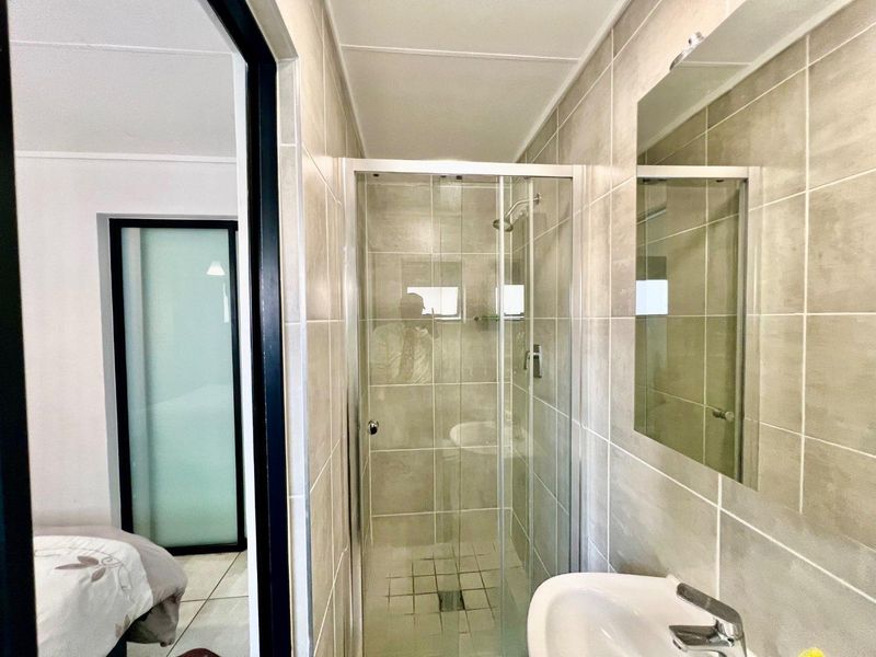 A clean, modern bathroom featuring a glass-enclosed shower, pedestal basin with mixer tap, and neutral wall tiling.