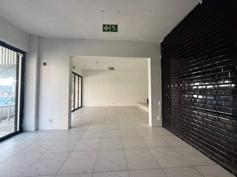 Spacious open-plan retail area featuring white tiled flooring, a striking black subway tile feature wall, and large glass windows for excellent street visibility.