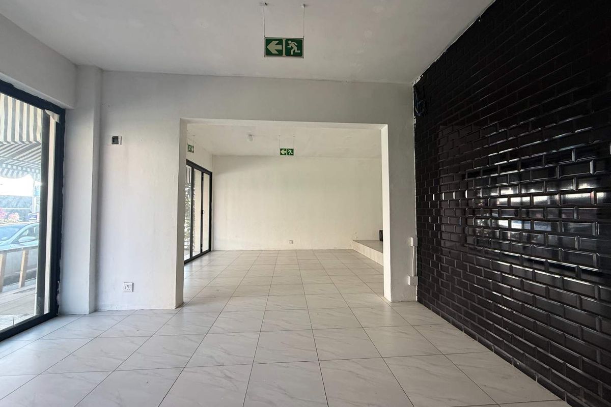 Spacious open-plan retail area featuring white tiled flooring, a striking black subway tile feature wall, and large glass windows for excellent street visibility.
