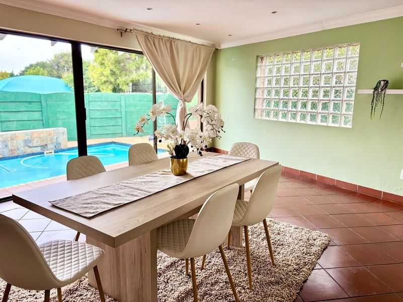 Bright dining room featuring tiled flooring, a decorative glass block window, and large sliding doors providing direct access to the outdoor pool area.