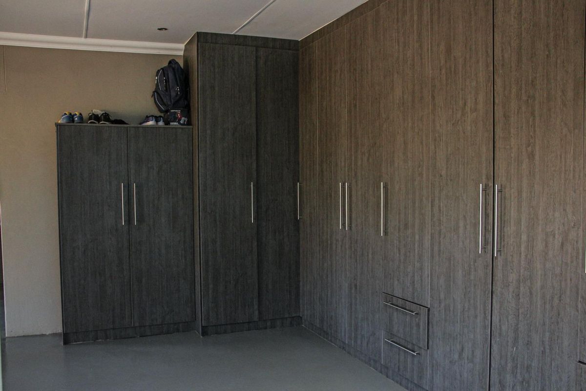 A bedroom featuring extensive dark wood-grain built-in cupboards providing ample storage space and neutral wall finishes.