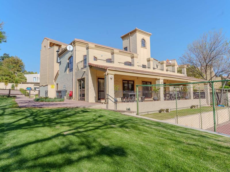Rear view of a multi-story apartment building featuring a covered patio, upper-level balconies, and a well-maintained lawn area.