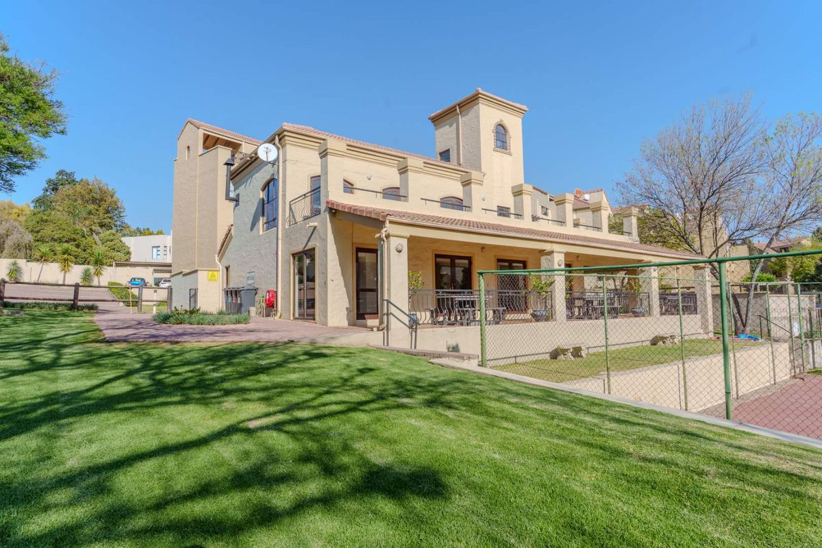 Rear view of a multi-story apartment building featuring a covered patio, upper-level balconies, and a well-maintained lawn area.