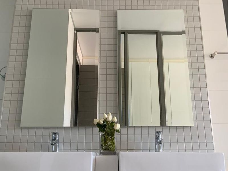 A modern bathroom featuring a double vanity with white basins, chrome fixtures, and a clean mosaic-tiled wall backdrop.