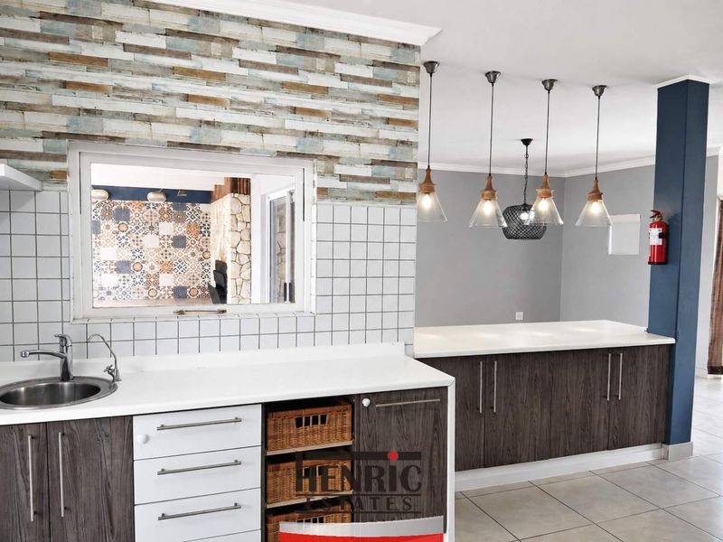 Modern kitchen featuring dark wood-look cabinetry, stone countertops, tiled splashback, and stylish pendant lighting, with a convenient pass-through window to the adjacent living area.