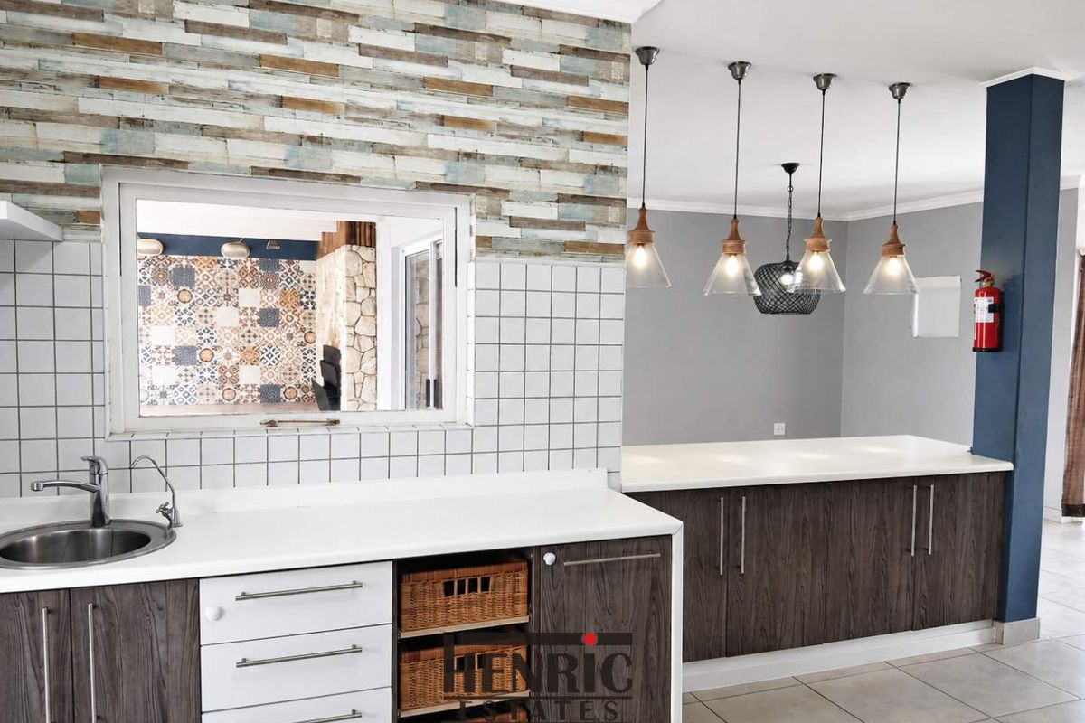 Modern kitchen featuring dark wood-look cabinetry, stone countertops, tiled splashback, and stylish pendant lighting, with a convenient pass-through window to the adjacent living area.