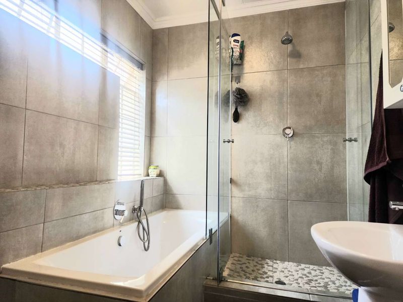 Modern bathroom featuring a built-in bathtub, a separate glass-enclosed shower with mosaic flooring, and neutral wall tiling.