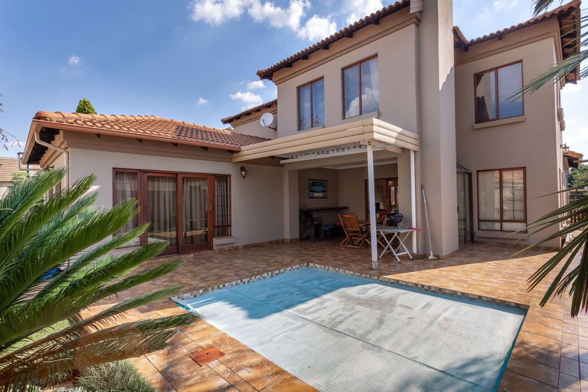 Rear exterior view featuring a tiled patio area, a covered outdoor entertainment space, and a swimming pool with a protective cover.