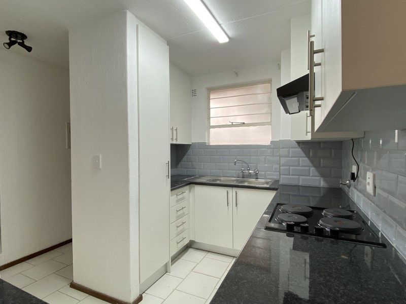 A clean, functional kitchen featuring white cabinetry, dark granite countertops, a grey subway tile backsplash, and integrated electric hob with extractor fan.