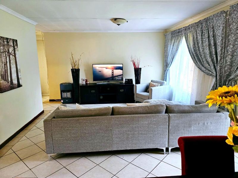 A comfortable living room featuring tiled flooring, neutral walls, and natural light through large windows with curtains.
