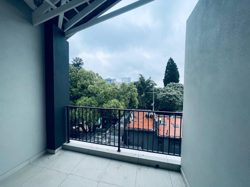 A covered balcony featuring tiled flooring, a metal balustrade, and exposed roof rafters, offering an elevated view of the surrounding neighborhood and greenery.