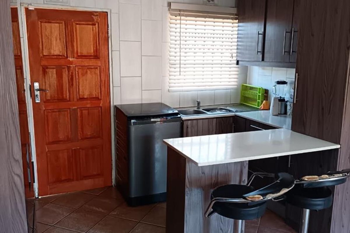 Compact kitchen featuring dark wood-look cabinetry, a breakfast bar, tiled flooring, and a functional sink area with natural light from the window.