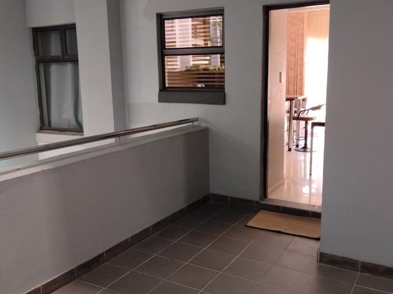 A covered balcony area featuring tiled flooring and a stainless steel balustrade, providing an outdoor transition space into the apartment interior.