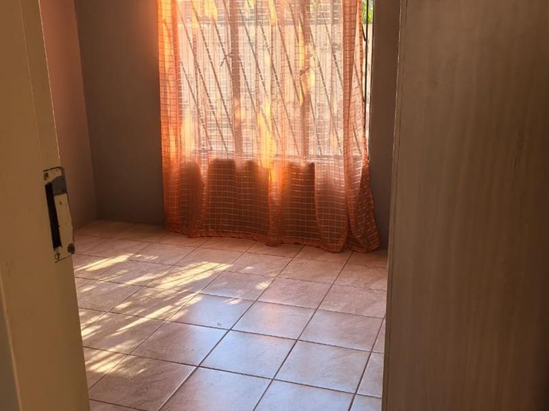 A bright, empty bedroom featuring tiled flooring and a built-in cupboard, offering a clean canvas for personalization.