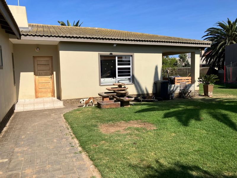 Rear view of the house featuring a paved walkway, covered patio area, and a lawn with established garden elements.