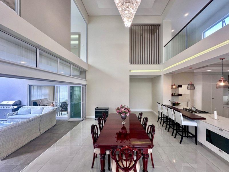 Spacious open-plan living and dining area featuring double-volume ceilings, modern kitchen island, sleek porcelain tiling, and seamless indoor-outdoor flow through folding glass doors.