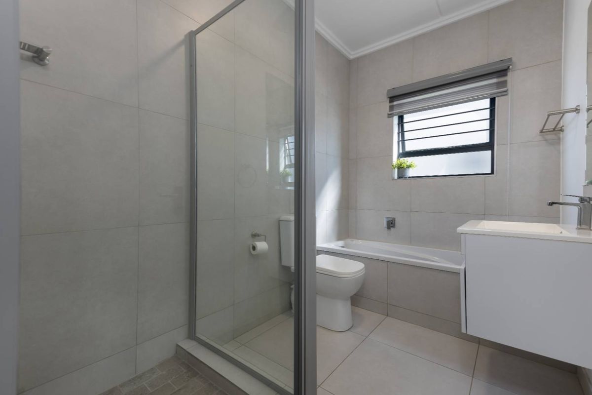 Modern bathroom featuring a glass-enclosed shower, a built-in bathtub, a vanity basin, and neutral floor-to-ceiling tiling.