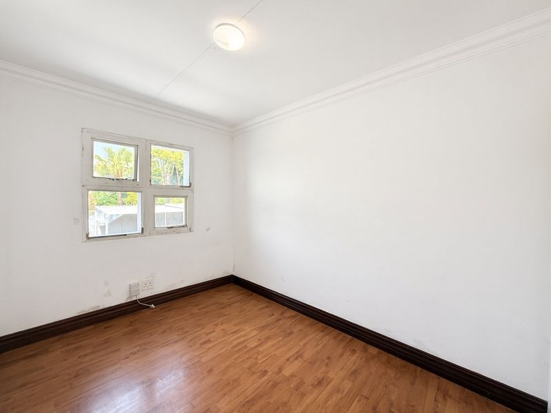 An empty bedroom featuring laminate flooring, dark skirting boards, and a multi-pane casement window, ready for a fresh coat of paint and new styling.